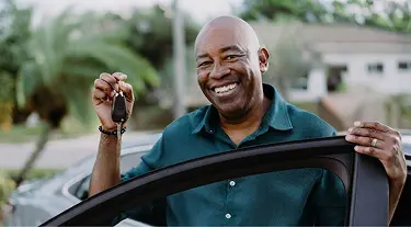 Man smiling, holding car keys, about to get in a car