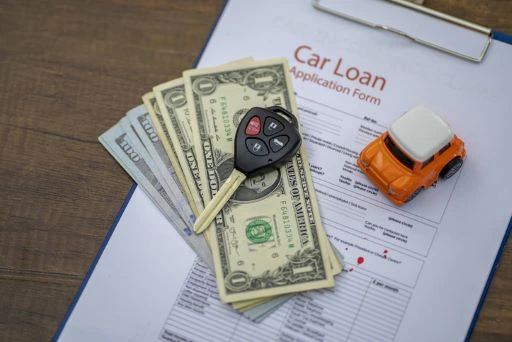 Car keys, cash and a toy car on top of a car loan application.